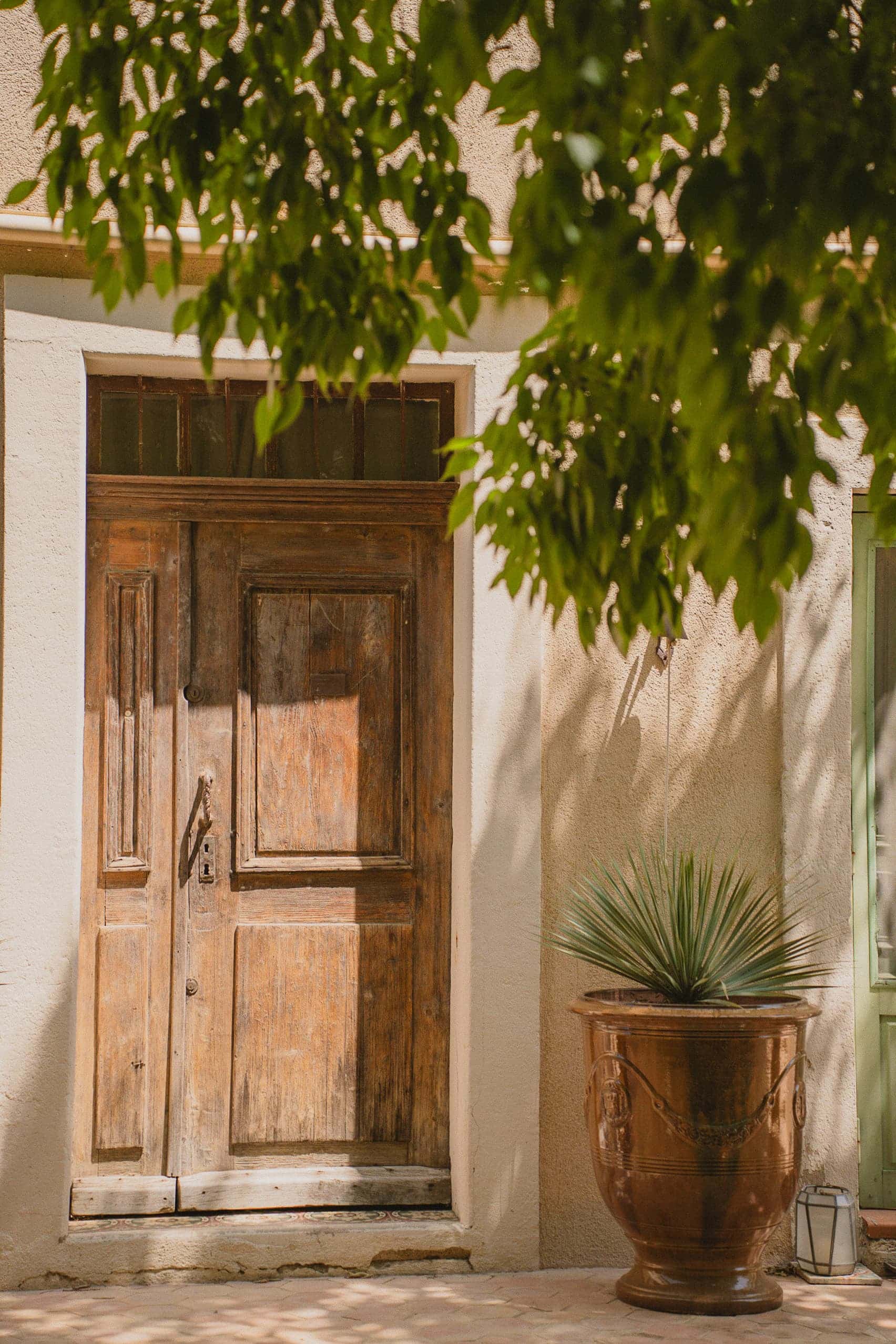 Entrée de La Roucoulade, maison de charme à Ventabren en Provence, avec porte ancienne en bois, murs clairs et végétation méditerranéenne.